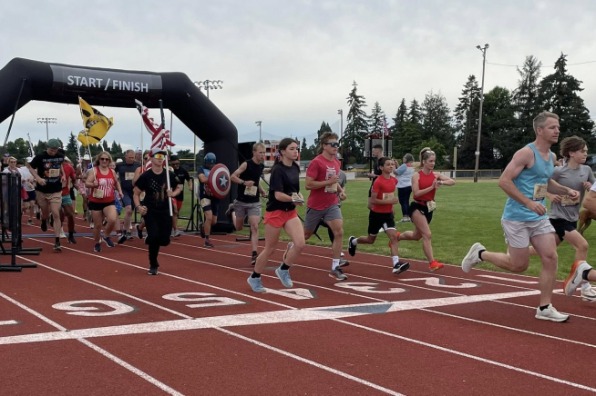 A group of runners participating in a race on an outdoor track, passing under a black inflatable arch labeled "START / FINISH."