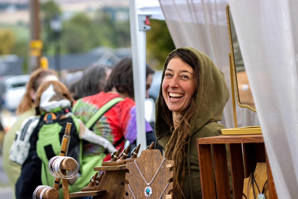 Vendor sells jewelry beneath a tent at an outdoor festival.