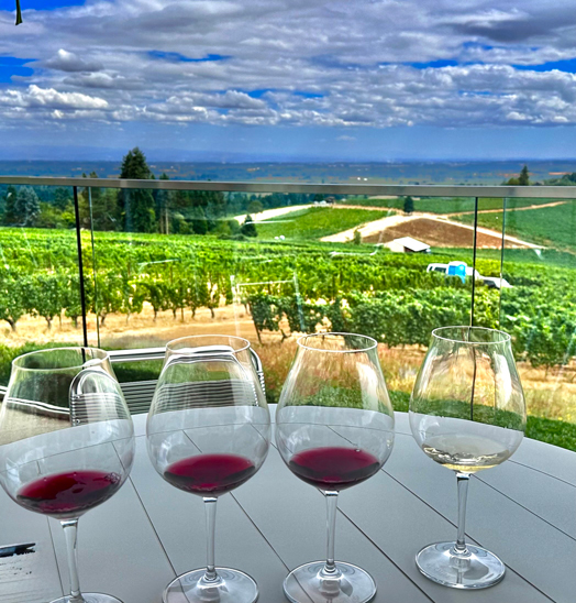 a flight of four wines in stemmed wineglasses on a table overlooking a vineyard in Oregon's Willamette Valley
