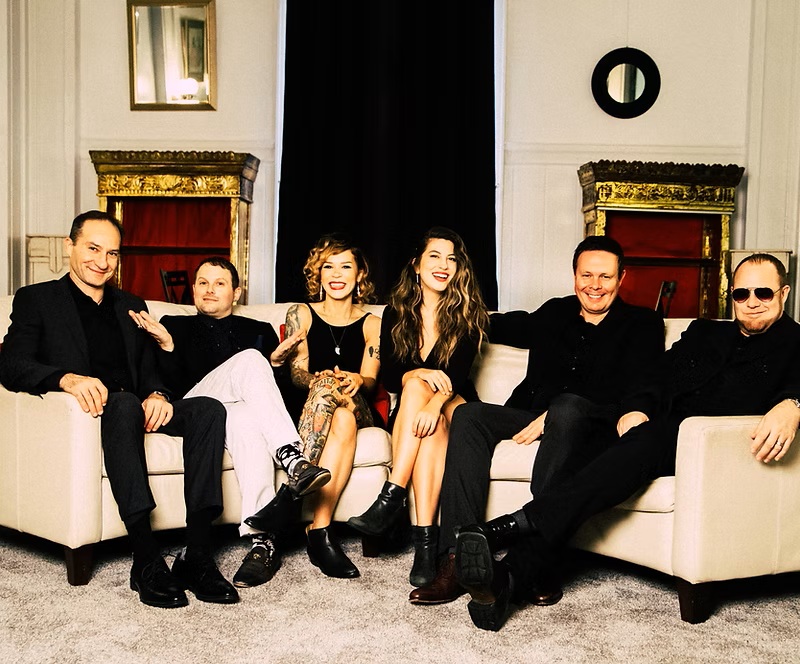 Six people dressed in mostly black site on a large couch.