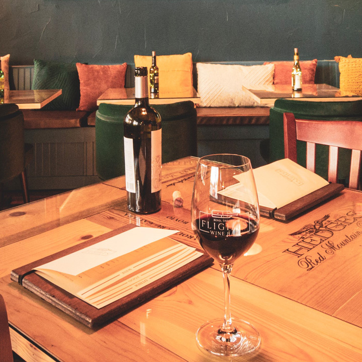 wine glass containing red wine with wine bottle and menus placed on wooden table with booth seating in background