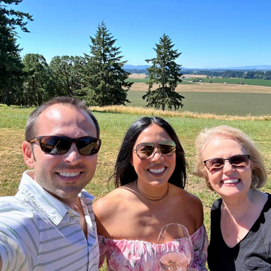 selfie of three people wearing sunglasses outside. one holds wine glass