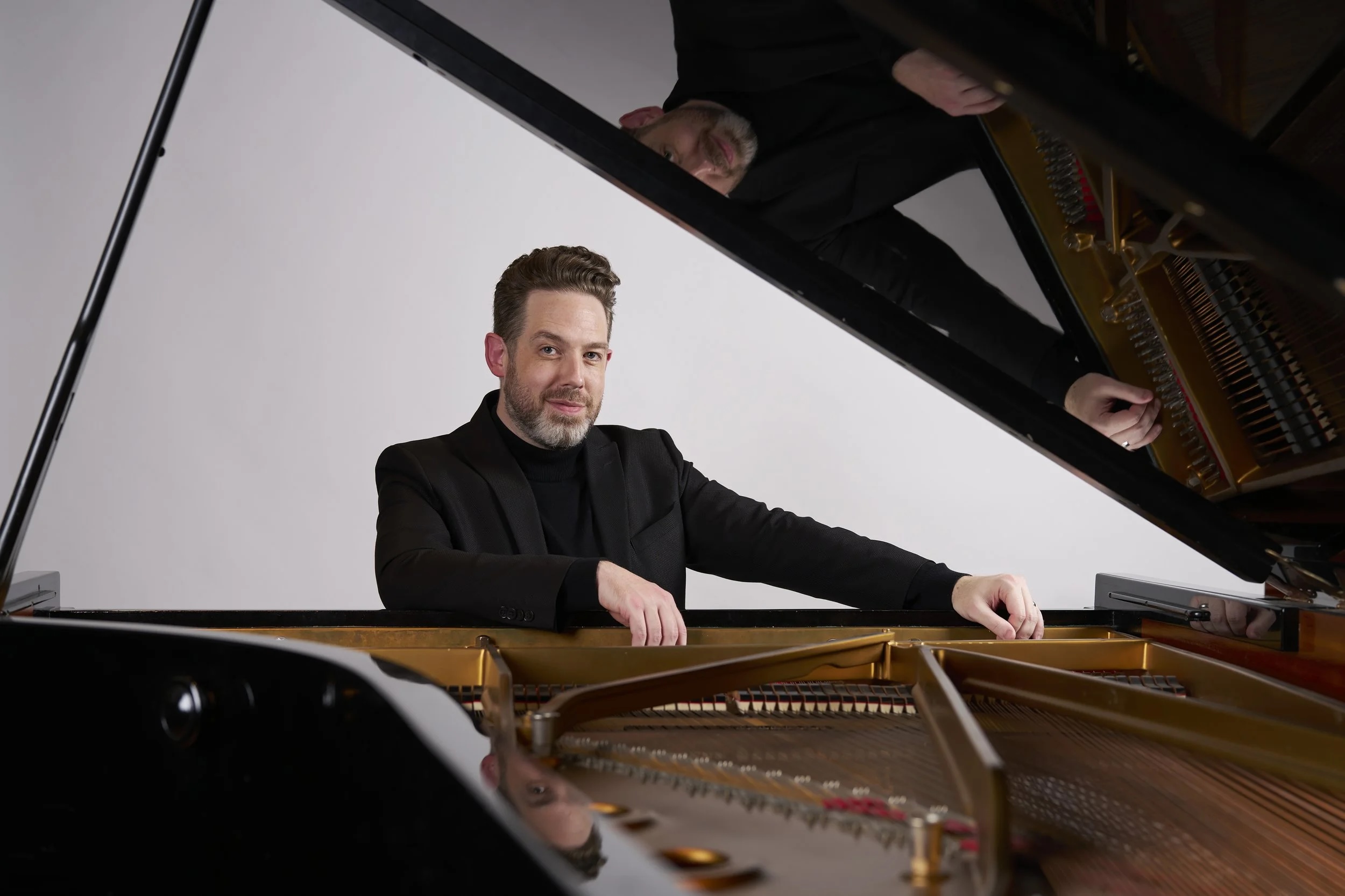 bearded man sits at grand piano