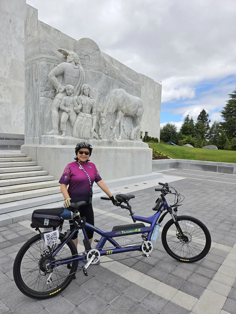 Woman with tandem e-bike in front of outdoor sculpture.