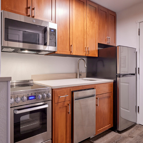 kitchen of hotel room with microwave, range, dishwasher, sink and refrigerator