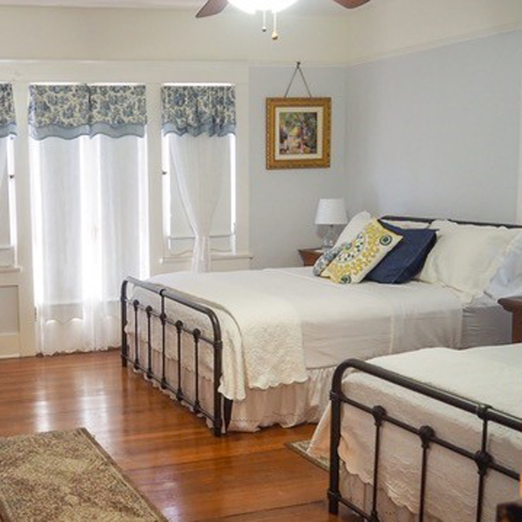 interior of guest room of bed and breakfast with hardwood floors, two double beds and windows