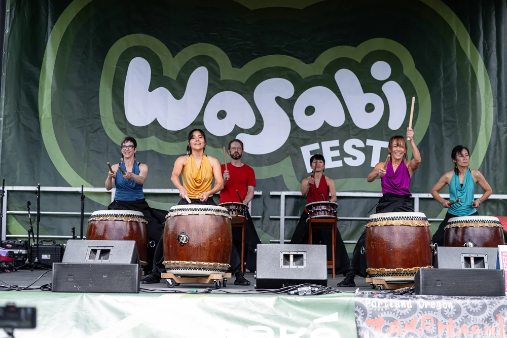 Five performers playing large traditional Japanese taiko drums on stage at Wasabi Fest.