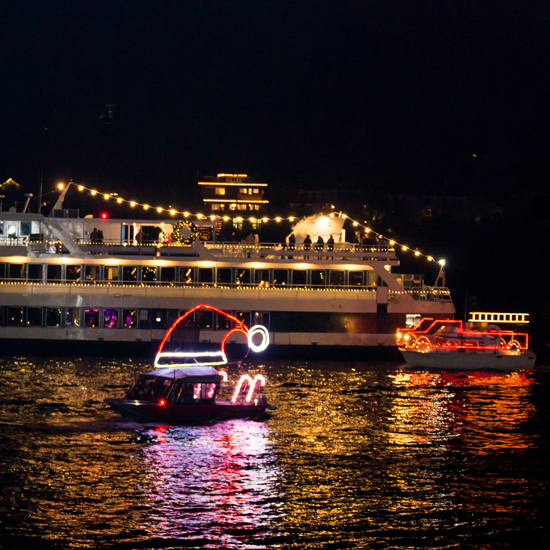 two small boats decorated for a holiday light parade in front of larger vessel
