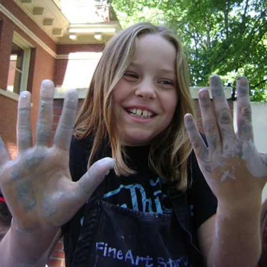 child smiling and holding up clay covered hands