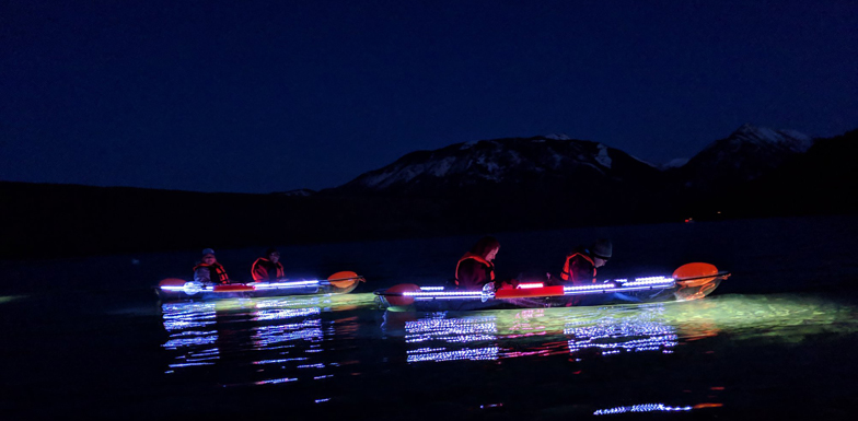 two kayaks with two people each float on a lake at night