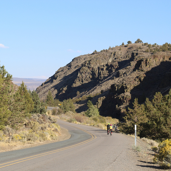 two bicyclists in distance ride on the road through scenic route