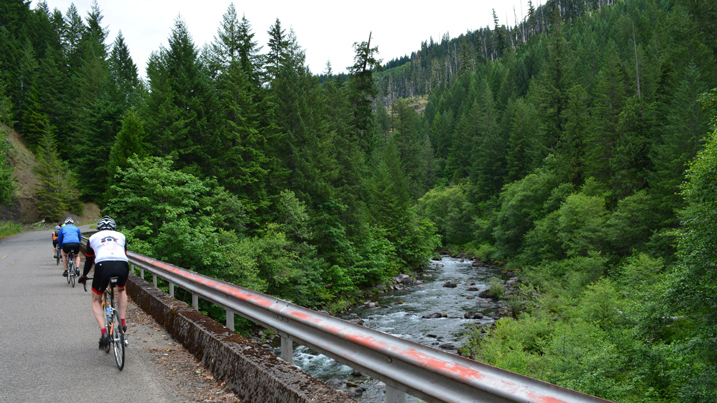 Group of bicyclists ride over a bridge with view of river below.