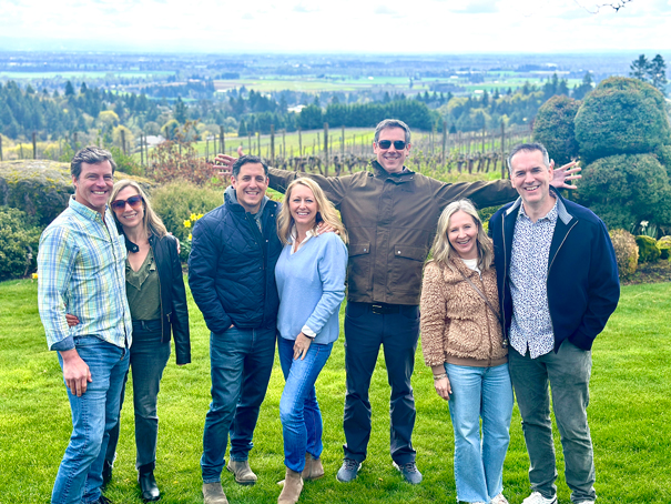 seven people pose in front of a vineyard