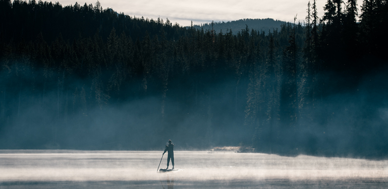 person on stand up paddle board in lake on foggy day