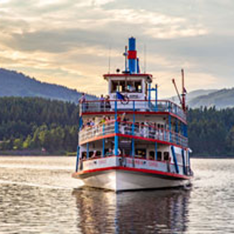 front view of riverboat on water with evergreen trees in background