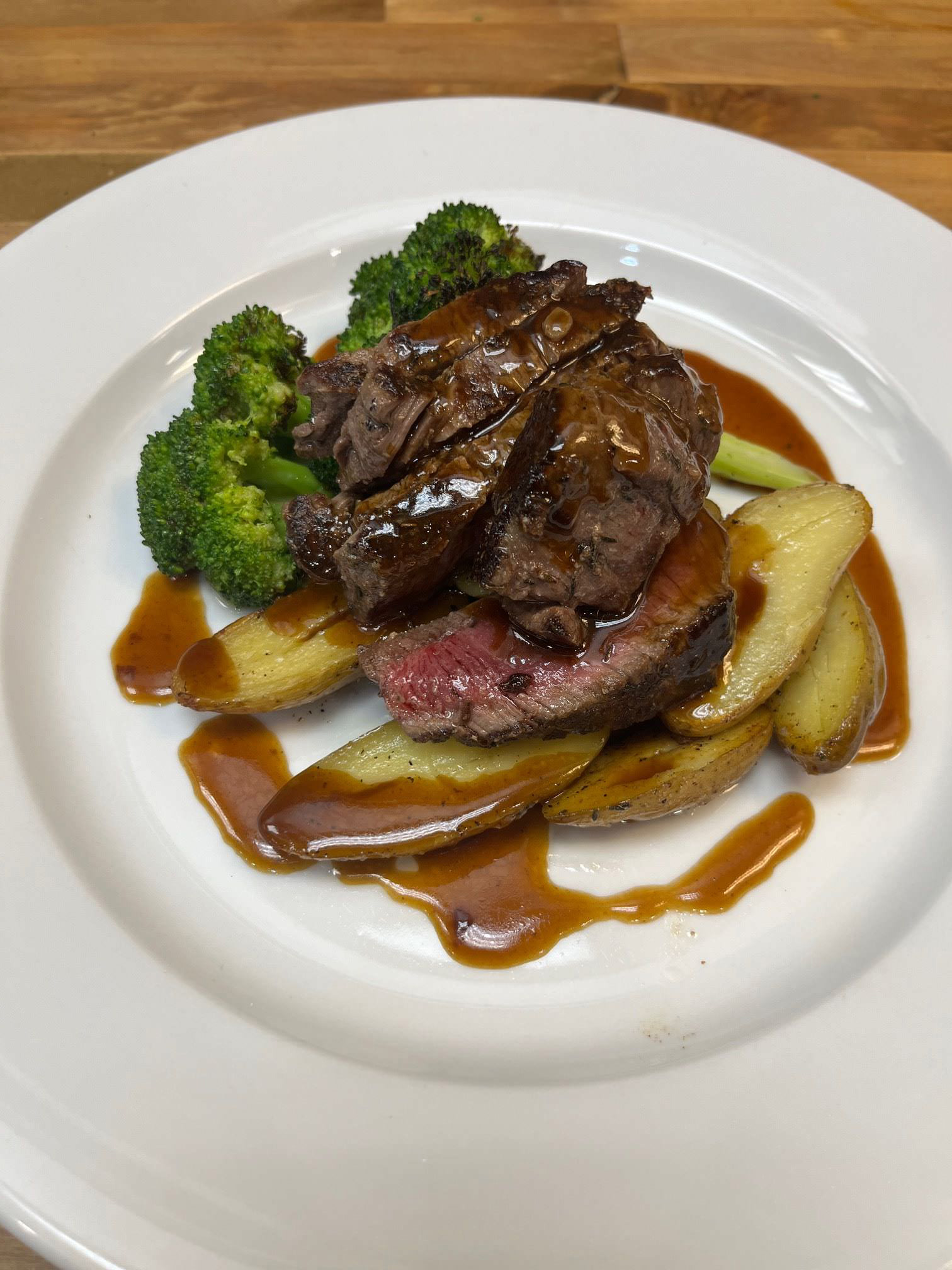 sliced steak atop potatoes and broccoli on a plate