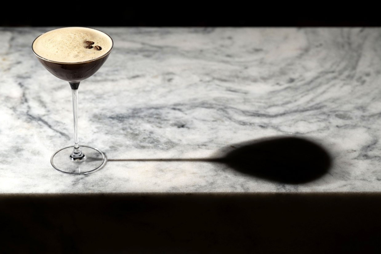 An espresso martini cocktail in a clear stemmed glass placed on a marble surface.