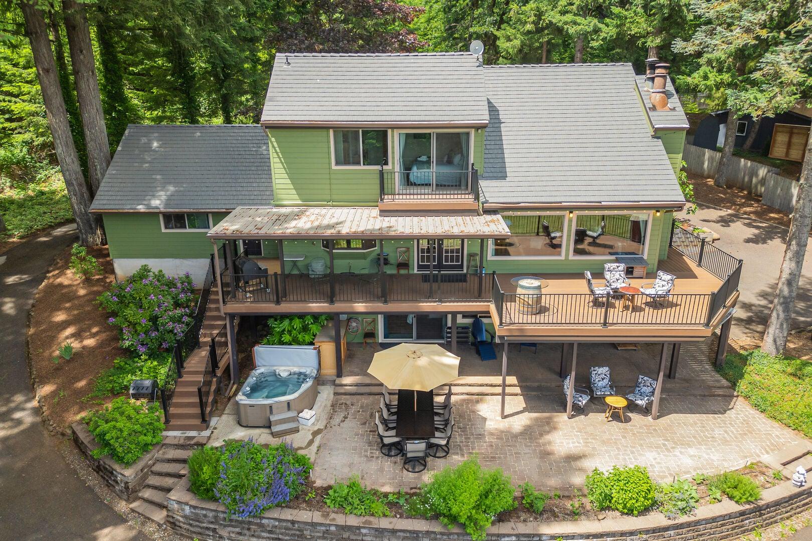 two-story green house with outdoor decks and a spacious patio area surrounded by trees.