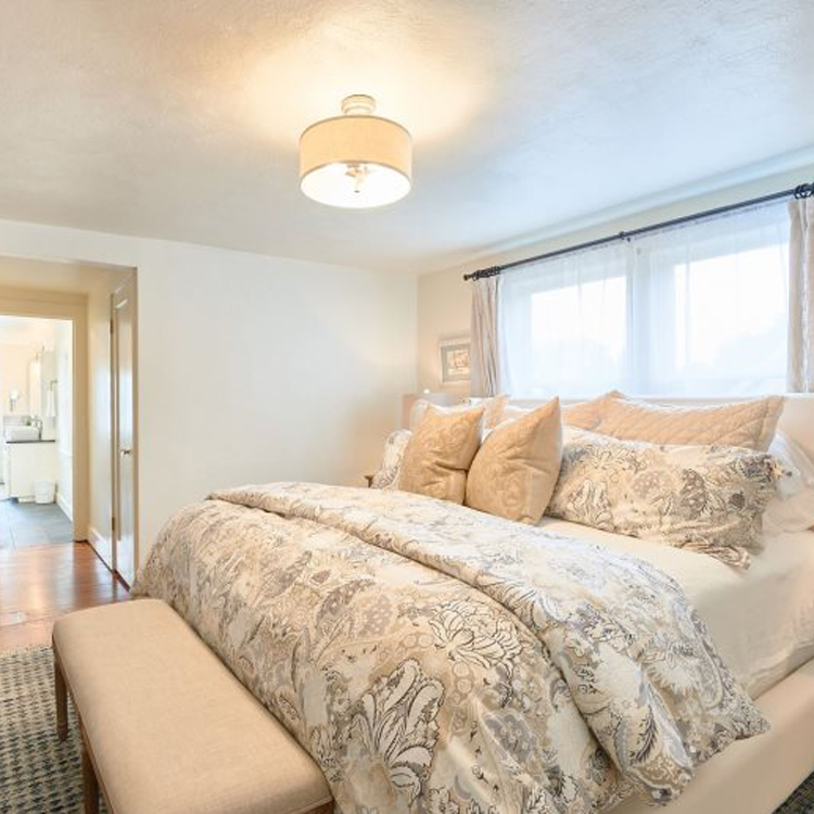 bedroom with sunlight coming in through windows, bench at foot of bed and en suite