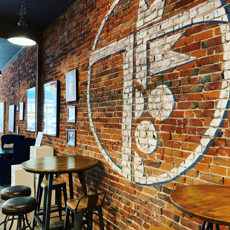 tasting room with tall tables and stools with orange brick walls with logo painting on it