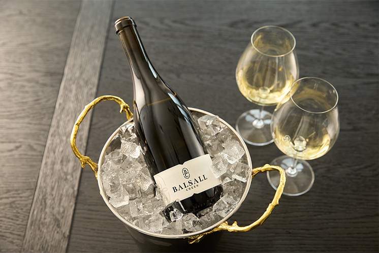 bottle of Balsall Creek wine on ice next to two stemmed wine glasses