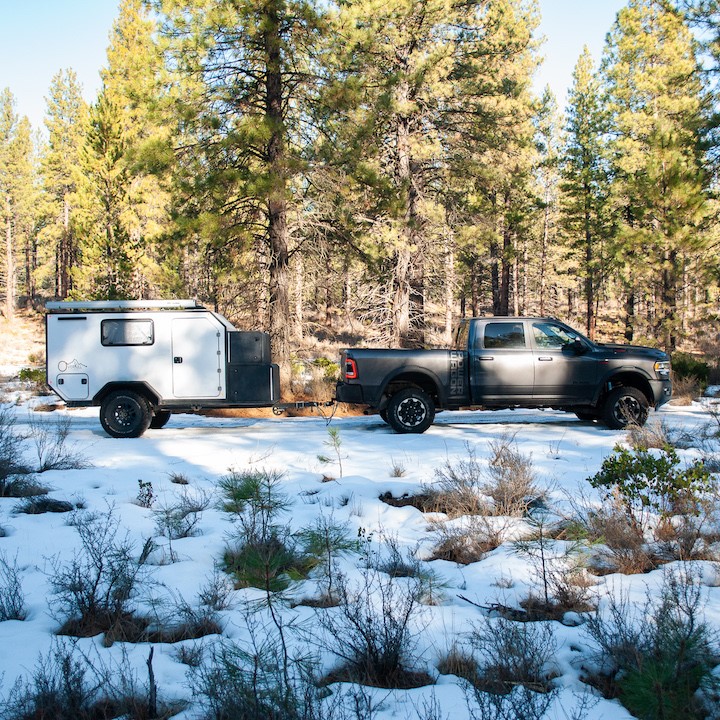 camp trailer hitched to truck in snow covered woods