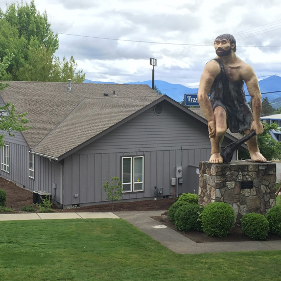 exterior of one story building with giant sculpture of a caveman in the courtyard