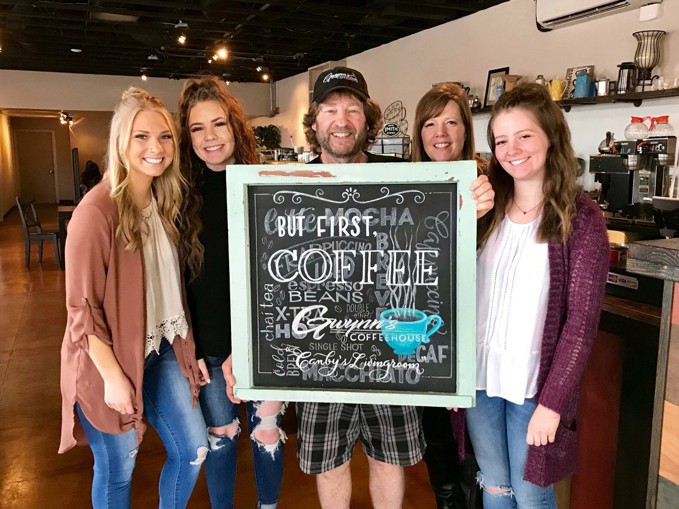 Five people standing with a coffee chalkboard sign.
