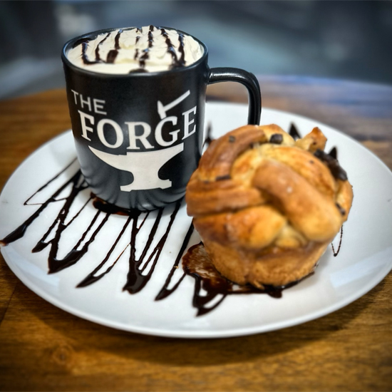 whipped cream topped beverage in mug on plate with a pastry and chocolate drizzle