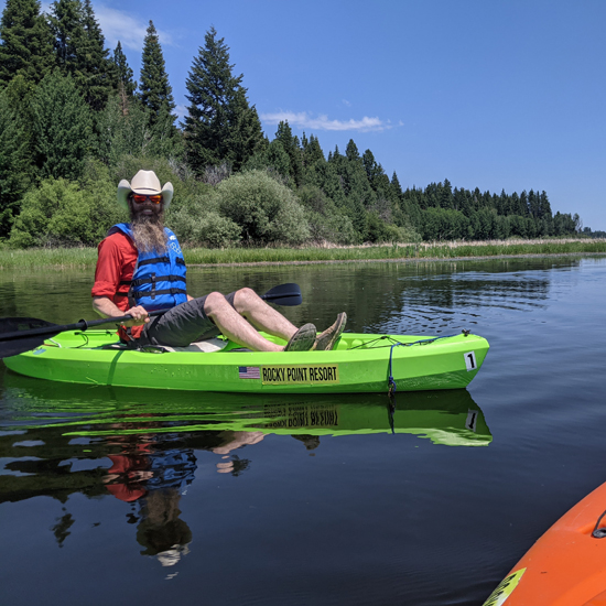 man with beard wearing cowboy hat and personal floatation device in kayak