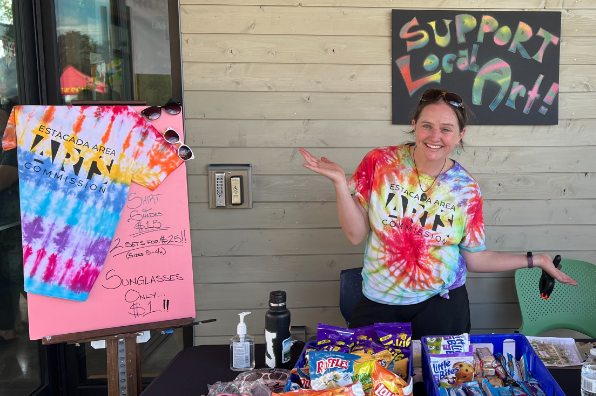 young woman wearing a tie dyed shirt stands in a vendor booth for Estacada Arts Commission