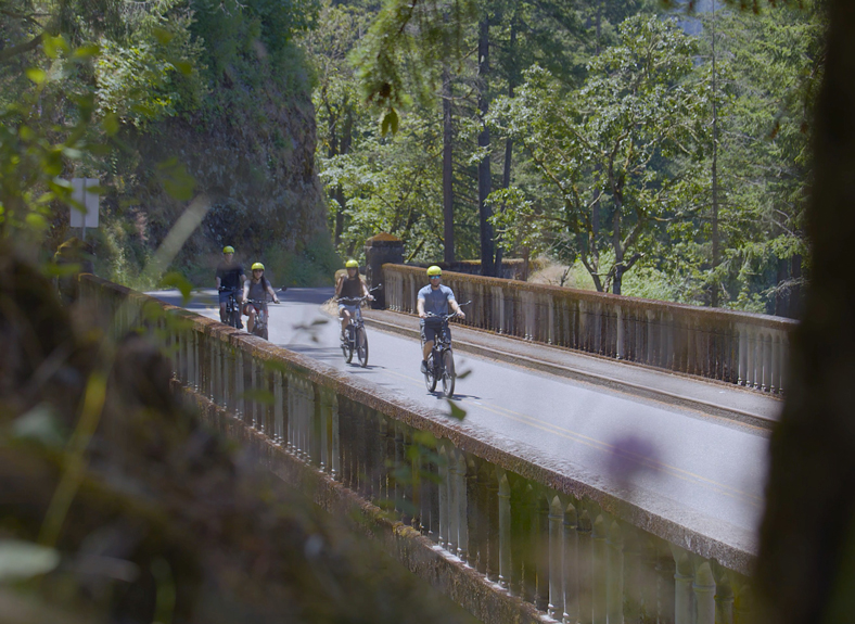 four people ride ebikes across a bridge