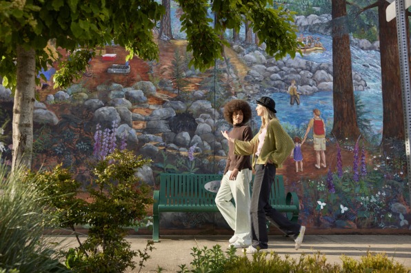 Two people walk on sidewalk in front of a mural.