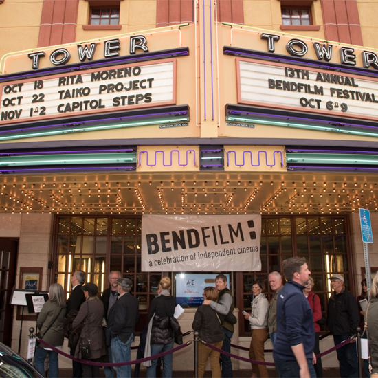 crowd standing in a line outside of a movie theater with banner for BendFilm hanging behind them