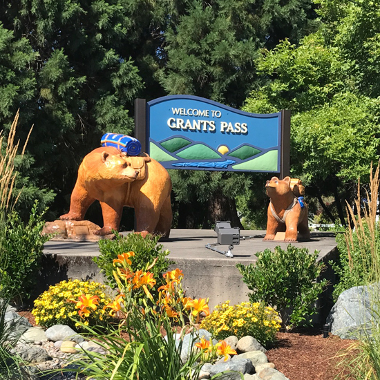 decorative sign with text for Welcome to Grants Pass with a bear sculpture on each side of sign