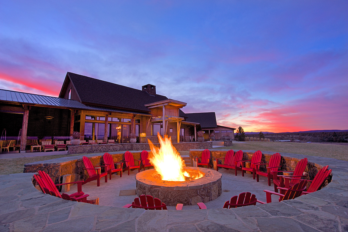Sunset with fire pit and chairs around a lodge.