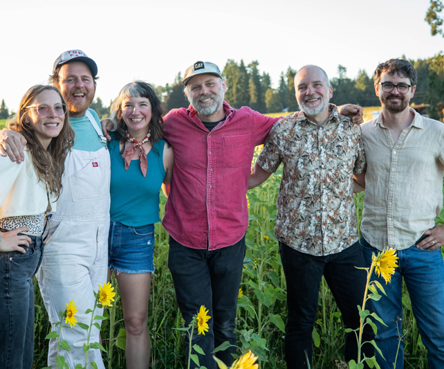 group of people smiling while standing in a sunflower field