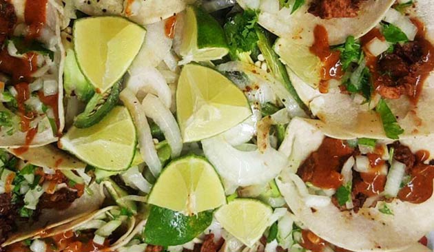 Close-up of tacos with lime, onions, and red sauce.