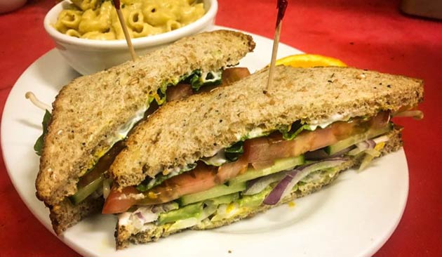 Sandwich with lettuce, tomato, cucumber, and onion on a white plate.