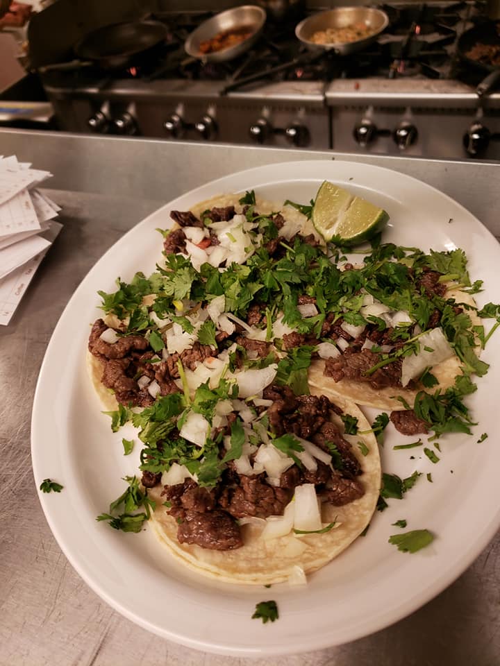 Plate with three tacos topped with onions, cilantro, and lime.