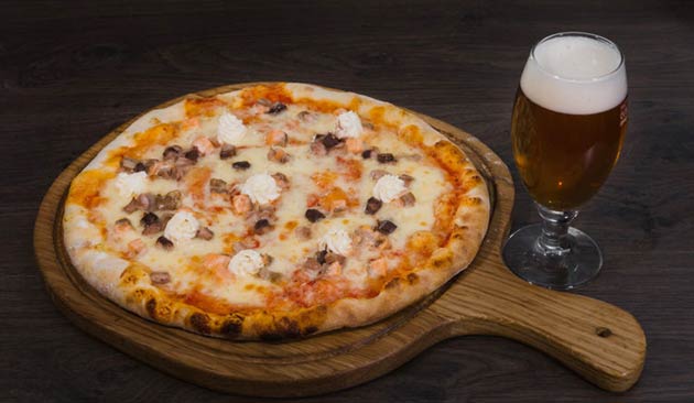 Pizza with seafood toppings next to a glass of beer.