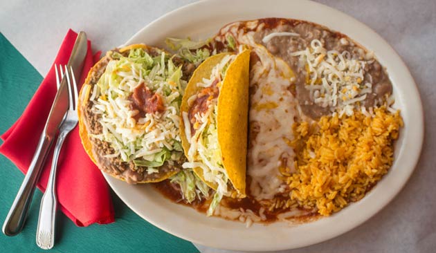 Plate with tacos, beans, and rice on green cloth.