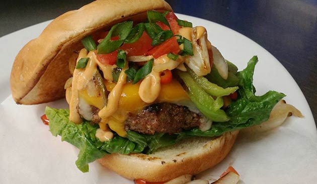 Cheeseburger with lettuce, tomato, and peppers on a white plate.