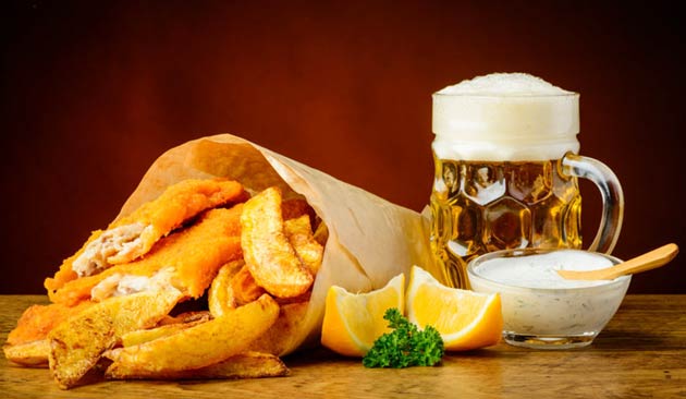 Fried fish, beer, and lemons on a wooden table.
