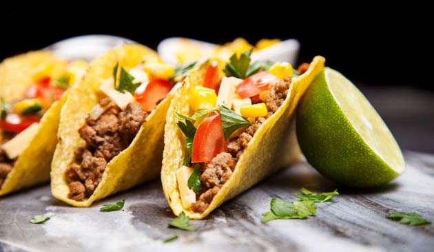 three hard shell tacos next to half of a lime