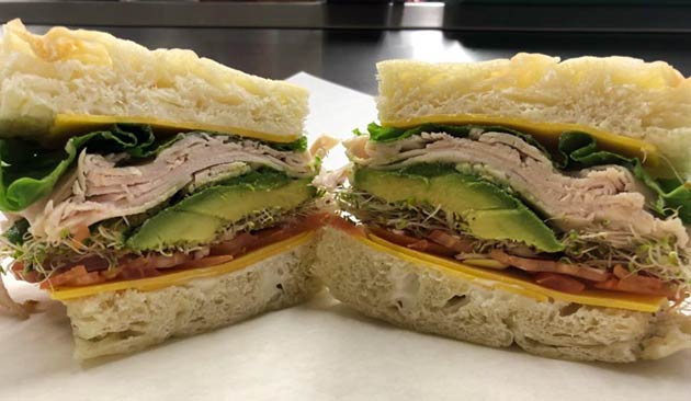 Half a sandwich with turkey, avocado, lettuce, and sprouts.