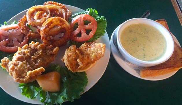 Fried food platter with onion rings, lettuce, and soup on a saucer.