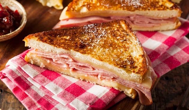 Grilled ham and cheese sandwich on a red and white checkered napkin.