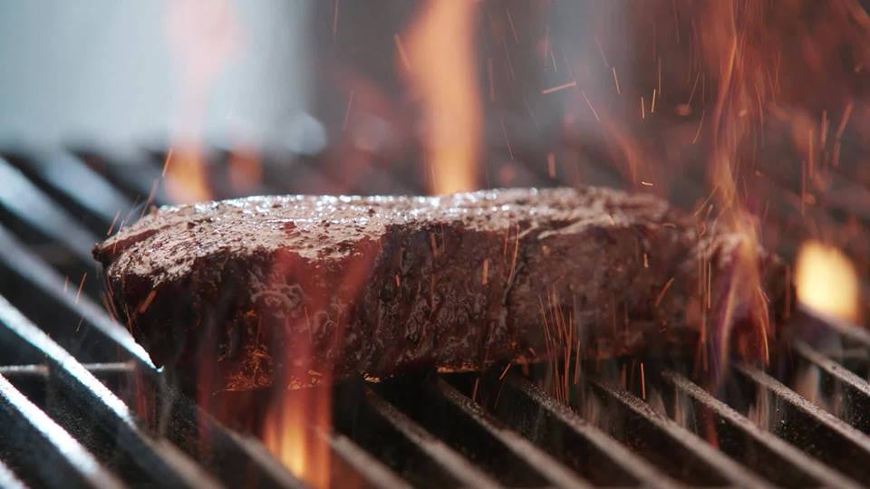 Steak cooking on a hot grill with flames.