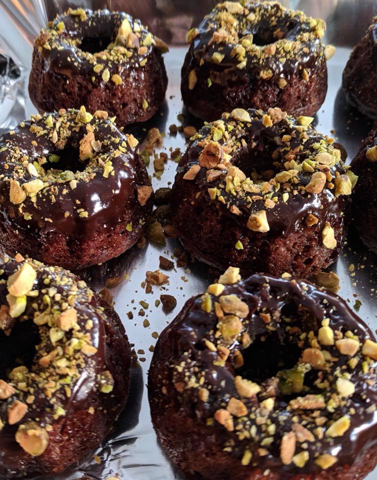tray of chocolate doughnuts with glaze and chopped nuts on top